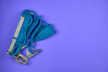 Mor arka planda tırmanma koşumları. Dağcılık için teçhizat, üst manzara. Yükseklerde çalışmak için emniyet kemeri ekipmanları.