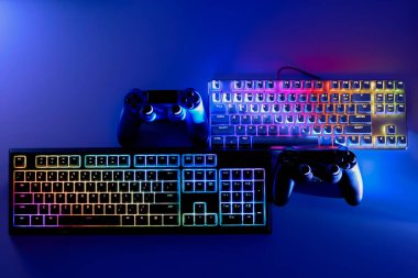 Oyuncuların çalışma alanı, üst manzara. Esport ya da bilgisayar kulübü kavramı. Renkli klavyeler ve joystickler. Neon ışıkta oyun ekipmanları.