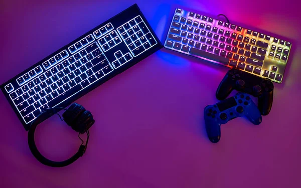 Gaming accessories for gaming, keyboards, joysticks and headphones. Keyboards with RGB light, top view. The gamer\'s workspace, in neon light