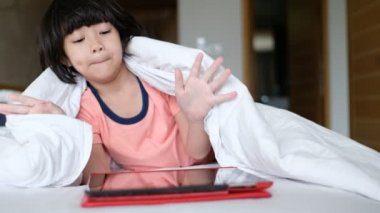 Çocuk yatakta tablet izliyor. 