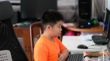 Asyalı çocuk evde bilgisayar öğreniyor, yeni normal. Mutlu çocuk ev ödevi yapıyor, uzaktan öğreniyor.