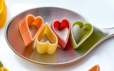 İtalyan makarnası şeklinde makarna kalbi. Turuncu, sarı, kırmızı, yeşil renkler. Tatil için yiyecek. Beyaz arkaplanda Sevgililer Günü 'nün aşk sembolü.