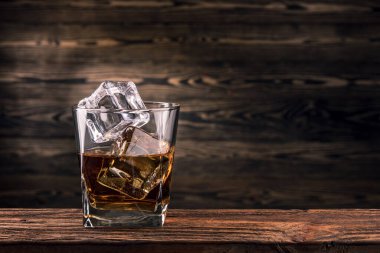 Bir bardak viski, burbon veya doğal ahşap arka planda buz küplü brendi. Lokantadaki bar tezgahında alkol içeceği. Kopyalama alanı olan makro fotoğraf. 