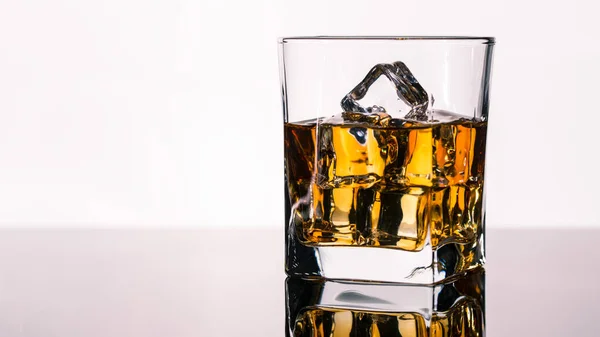 Glass of Whiskey, Bourbon or Brandy with ice cubes on table with reflection. Alcohol drink on Bar counter in the restaurant. Macro photo on white background with copy space.