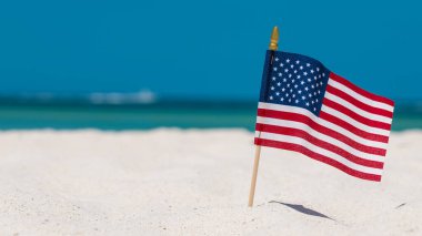 Sahildeki Amerikan Bayrağı. 4 Temmuz Bağımsızlık Günü. Amerikan yıldız çizgili vatanseverlik sembolü. Birleşik Devletler Tatilleri. Yaz tatilleri. Okyanus kumu. Parlak güneşli bir gün ve deniz tuzlu suyunun mavi rengi. 