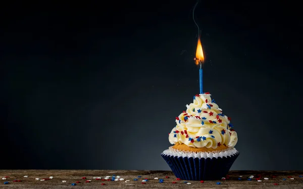 Birthday cupcake American style. 4th of July, Independence, Memorial or Presidents Day. Tasty cupcakes with white cream icing and colored stars sprinkles. Burning candle light in a cake. Sweet dessert