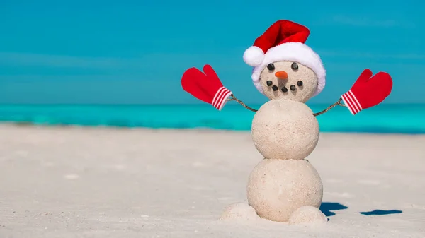 海滩上的雪人桑迪圣诞雪人 戴着红色圣诞老人帽 戴着手套或手套 在阳光灿烂的海滩上微笑雪人 新年快乐明信片的假日概念 佛罗里达冬季 海洋或海水 — 图库照片
