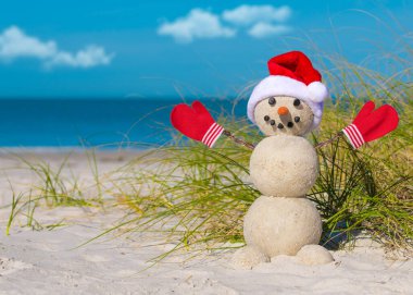 Kumsaldaki kardan adam. Noel Baba şapkalı, eldivenli, Noel Baba kardan adam. Güneşli sahilde gülen kardan adam. Mutlu yıllar kartpostalları için tatil konsepti. Florida Kışı. Okyanus beyazı kum.