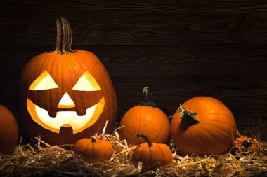 Cadılar Bayramı 'nda balkabağı oydum. Jack O Fenerler ve balkabakları. Korkunç Jack-o 'Lantern' in içinde yanan mumla aydınlatıcı. Tatil dekorasyonu. Mutlu Cadılar Bayramı. Hasır balya ve ahşap arka plan.