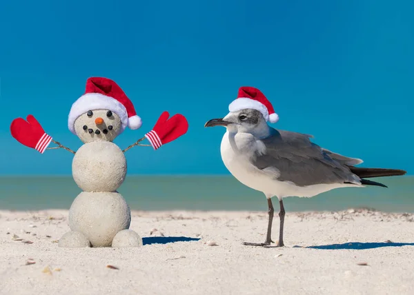 スノーマンとシーグルはビーチで 砂浜で赤いサンタの帽子のサンディクリスマスの雪だるまとカモメの鳥 日当たりの良いビーチで雪だるま 休日の概念 明けましておめでとうございます — ストック写真