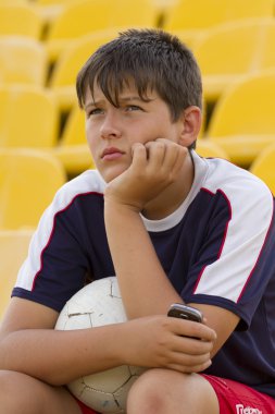 Üzgün çocuk futbol tribün üzerinde oturan bir top ile.