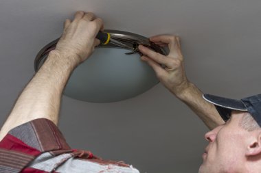 Electrician installs lighting the lamp on the ceiling of the room. clipart