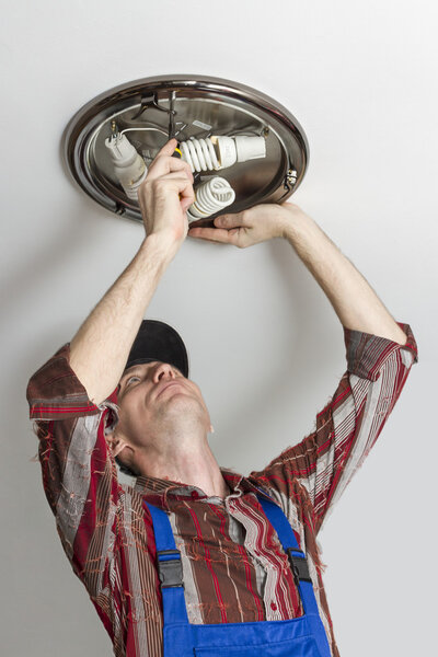 Electrician installs lighting the lamp on the ceiling of the room.