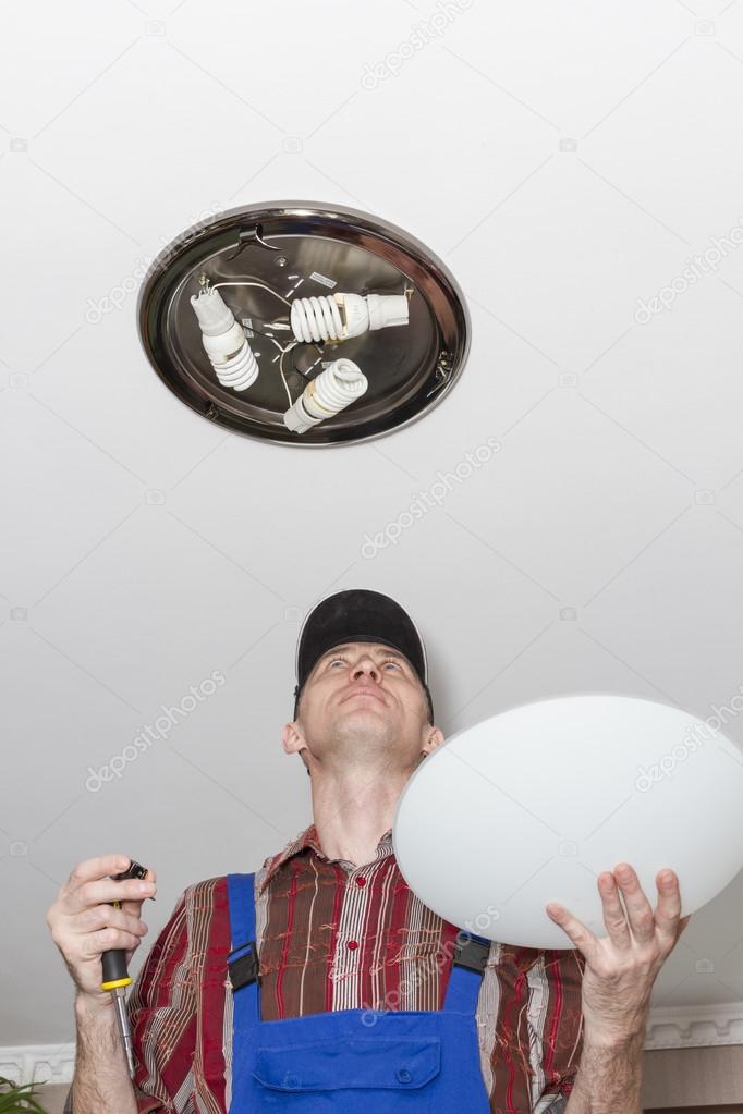 Electrician installs lighting the lamp on the ceiling of the room.