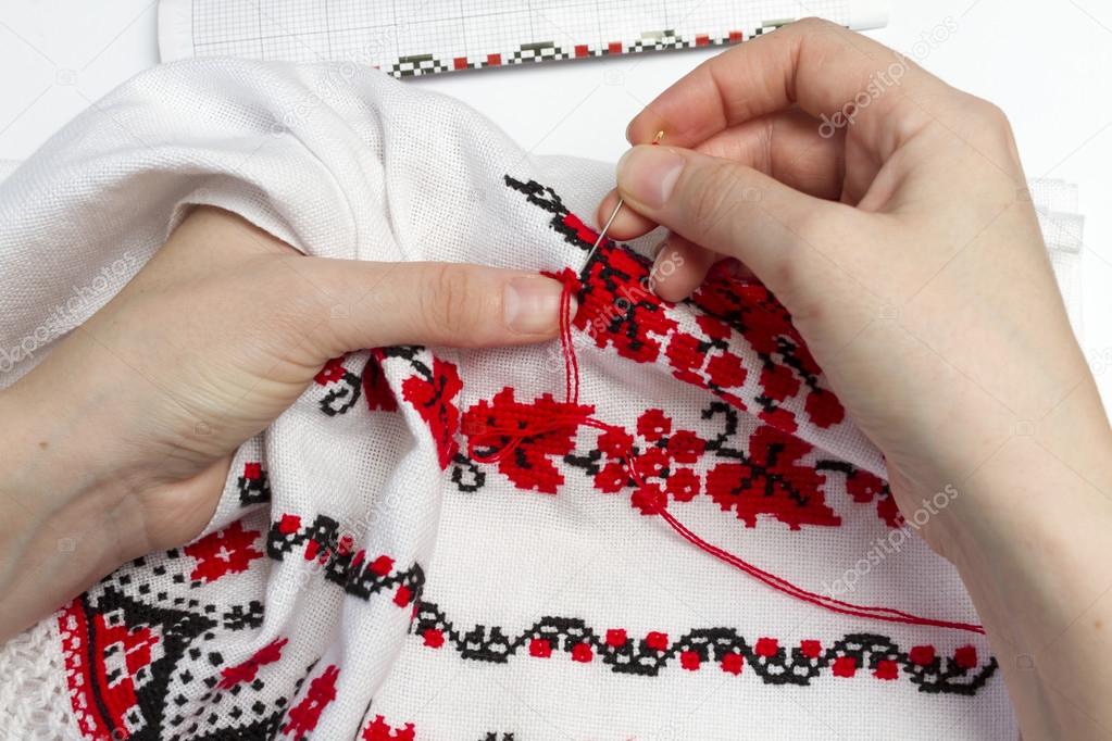 Woman embroiders national pattern red and black thread.