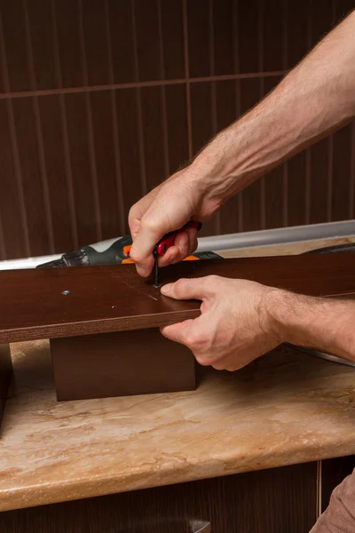 A man with a wrench in hand twists furniture.