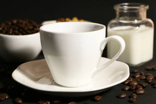 A cup of coffee with milk and coffee beans on a glass table. The concept of home comfort and warmth. On the table, a cup of coffee and a cake on a black background.