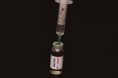 Coronavirus Covid-19 'la mücadele konsepti. Siyah arka planda, aşılı bir kavanoz ve şırınga var. Kavram: Hastalık, tıp, bilim.