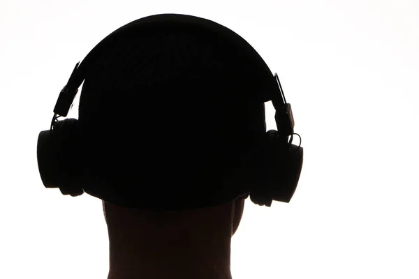 ワイヤレス技術 白い背景にヘッドフォンで暗い男性のシルエット ヘッドフォンの暗いシルエットは白い背景で音楽を聴く — ストック写真