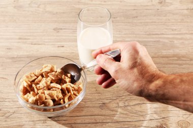 Sağlıklı yiyecekler. Kahvaltıyı mısır gevreği ve sütle yapan bir adam. Bir adam elinde bir kaşık, masada bir bardak süt tutuyor..