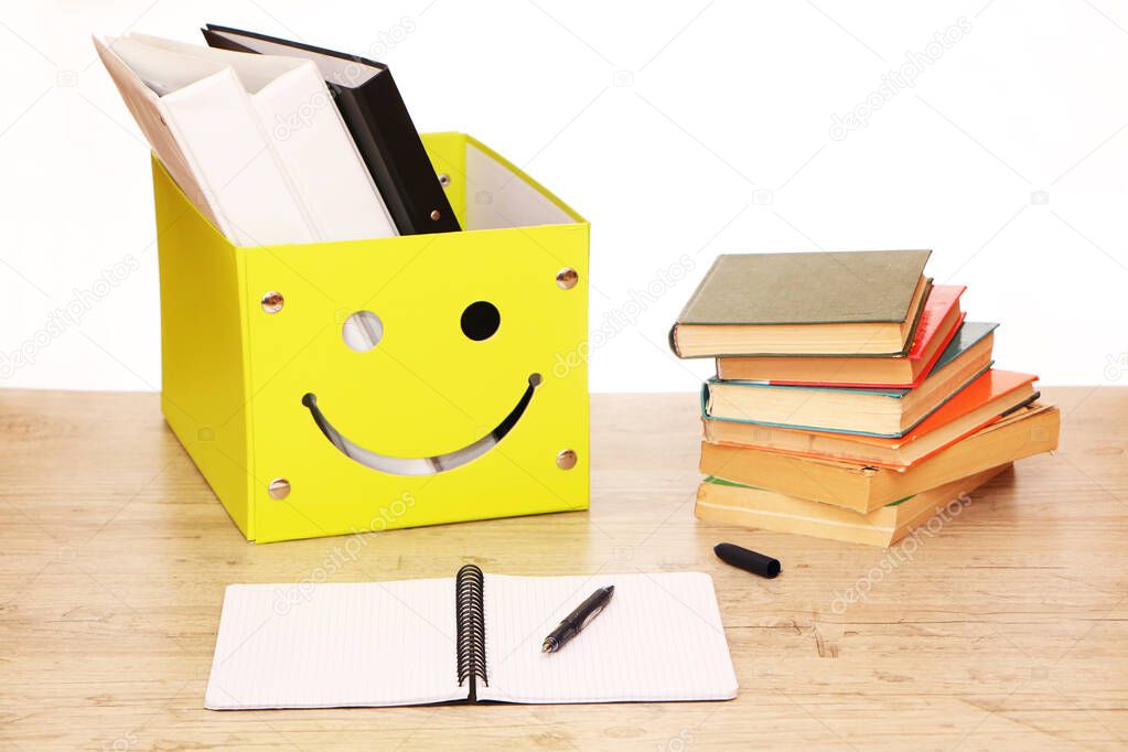 There is a yellow box on the table in the library with documents and research materials for the preparation of the report. Classroom teacher's desk with teaching materials.