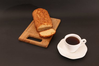 On a black background, a white cup with coffee and a sliced cupcake. Baking concept - dessert and coffee on a black background.