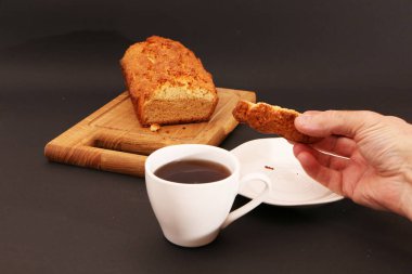 A man holds a cupcake in his hand and drinks coffee in a cafe for breakfast. A man is enjoying a dessert in a cafe.