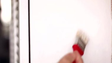 Bir adam eski bir dolabı fırçayla boyuyor. Elinde eski beyaz bir dolabın arka planına karşı kırmızı bir fırça tutuyor..