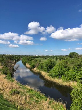 Idyllic Yaz Manzarası: Dramatik Bulutlu Gök Altında Nehir Akıyor. Canlı yeşil yaz yapraklarını ve mavi gökyüzünün ve bulutların güçlü kontrastını vurgular. Bir arkaplan ya da seyahat hedefi resmi olarak ideal.