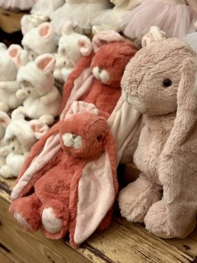 Ahşap bir rafta, pastel pembe ve terracotta renginde şirin pelüş tavşan oyuncakları..