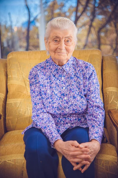 Oma zit in een gele stoel — Stockfoto