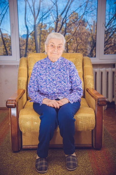 Oma zit in een gele stoel — Stockfoto