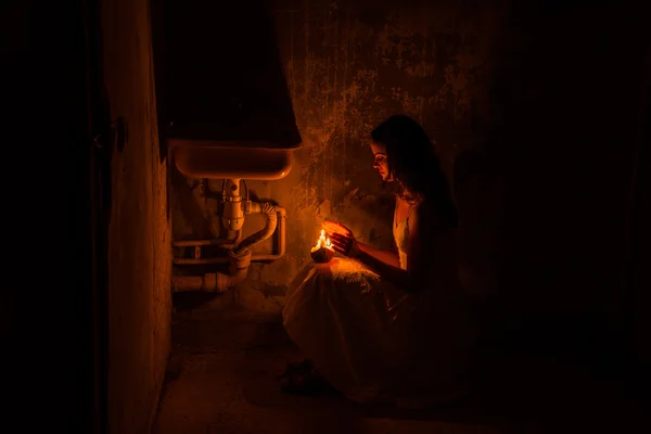 Dívka hřeje ruce s voskové svíčky. Opuštěný dům. — Stock fotografie
