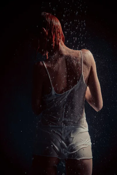 Chuveiro. Menina em uma camiseta branca em pé sob um chuveiro . — Fotografia de Stock