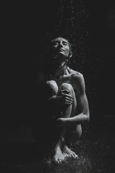 Una chica se sienta en el suelo bajo la lluvia. Fotografía en blanco y negro —  Fotos de Stock