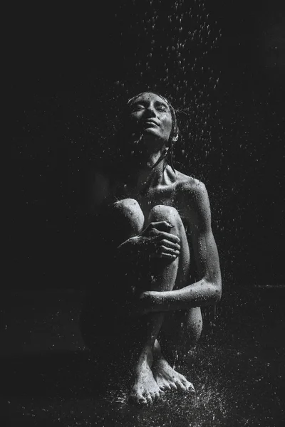 Una chica se sienta en el suelo bajo la lluvia. Fotografía en blanco y negro —  Fotos de Stock