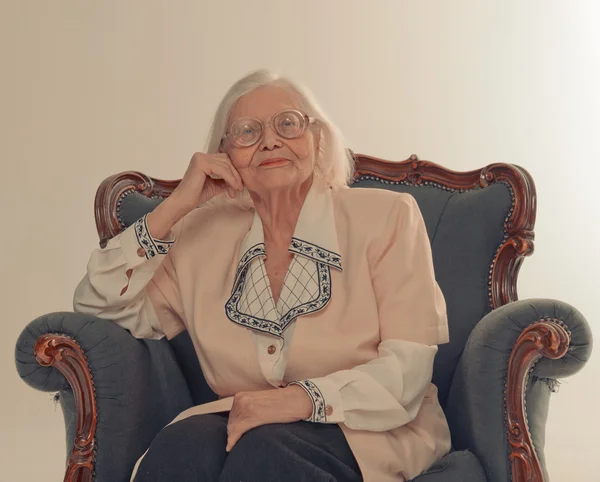 Büyükanne eski bir sandalyede oturuyor. Gülümsüyor. — Stok fotoğraf