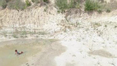 Güneş banyosu. Mayo giymiş bir kadın çölün ortasında küçük bir su birikintisinde yüzer. Hava görünümü