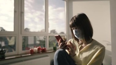 Tıbbi maske. Bir kadın tıbbi maske takıyor ve elinde cep telefonu tutuyor..