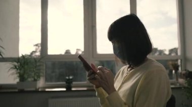 Tıbbi maske. Bir kadın tıbbi maske takıyor ve elinde cep telefonu tutuyor..