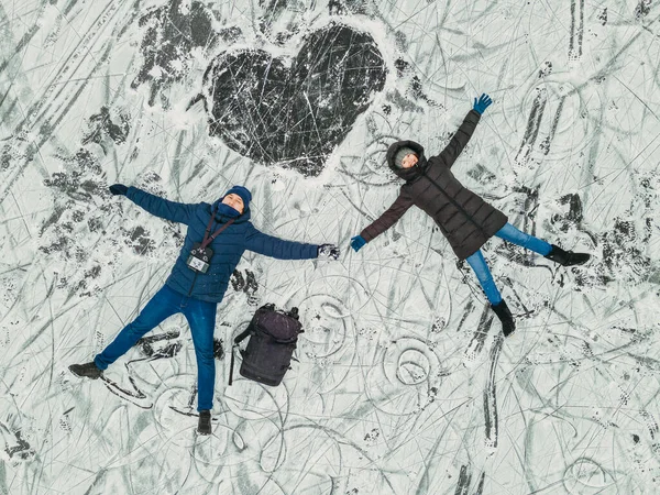 Heart. A man and a woman lie on the ice next to the painted whit. Aerial view.