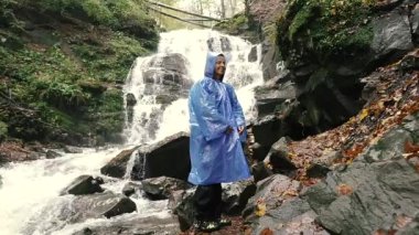 Yağmurluk. Yağmurluk giymiş bir kadın şelalenin arka planına atlıyor. Pylypets. Ukrayna.