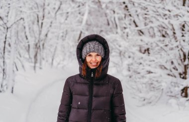 Kış. Karlı bir ormanın arka planında ceketli ve şapkalı bir kadın..