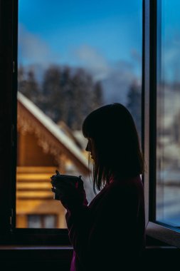 Kulübe. Penceredeki kadın sıcak bir içecek içiyor..