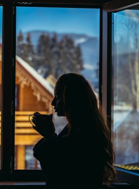 Kulübe. Penceredeki kadın sıcak bir içecek içiyor..