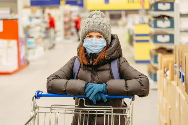 Grocery trolley. A woman stands with a grocery cart and a medical mask.