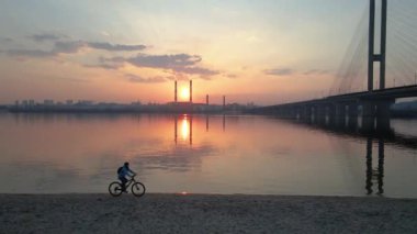 Bisiklet mi? Kadın, nehrin arka planına ve günbatımına karşı bisiklet sürüyor. Hava görünümü.