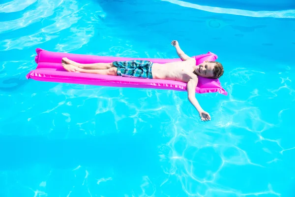 Ein Junge schwimmt auf einer aufblasbaren Matratze im Pool — Stockfoto