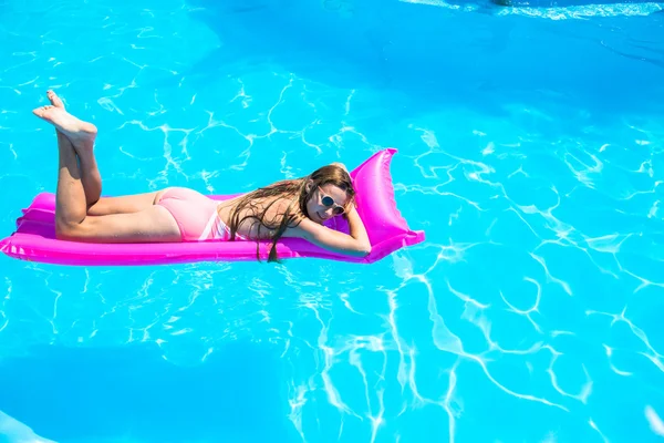 A menina flutua em um colchão inflável na piscina — Fotografia de Stock