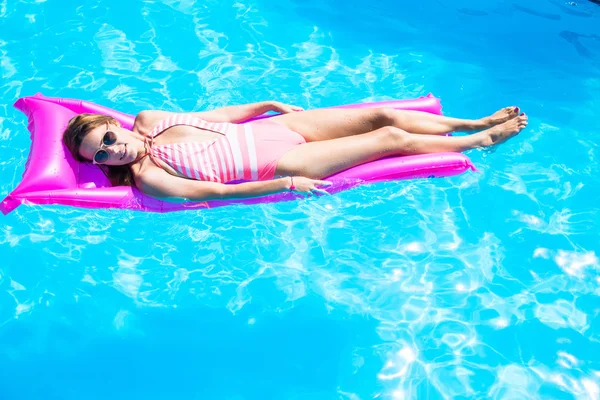 A menina flutua em um colchão inflável na piscina — Fotografia de Stock